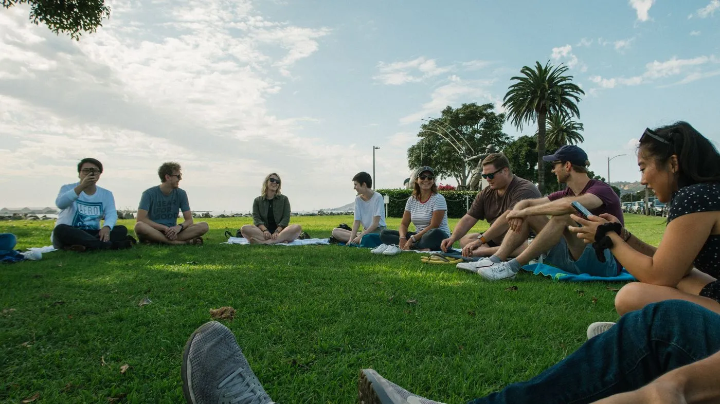 Un grupo de personas sentadas en ronda sobre el pasto, conversando al sol