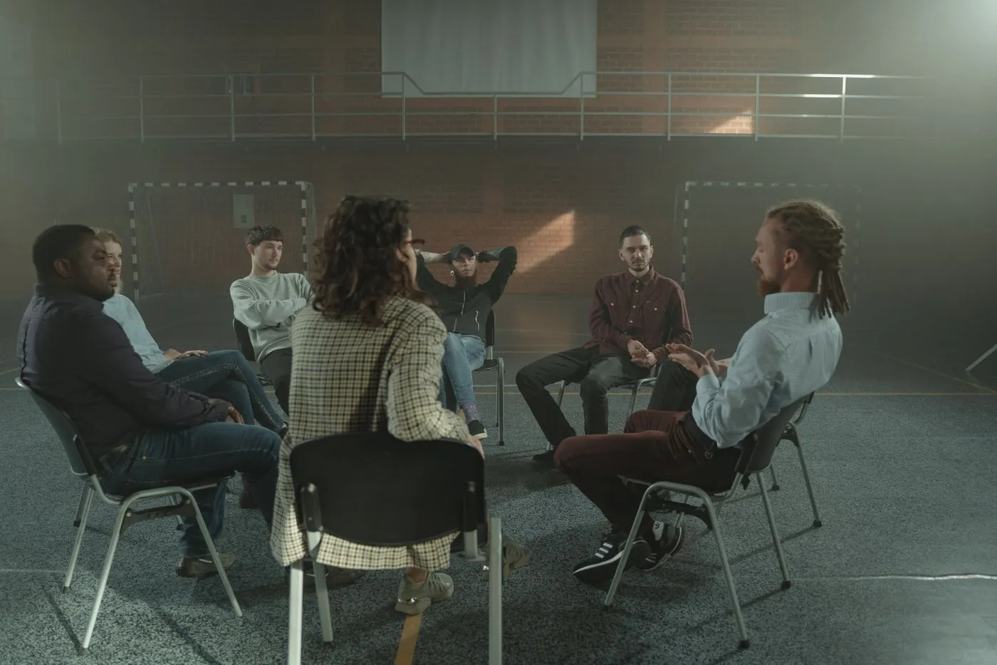Un grupo de personas sentadas en círculo en un salón, una de ellas habla